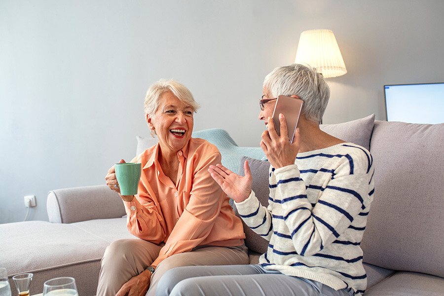 Seniorinnen sitzen lachend auf der Couch.