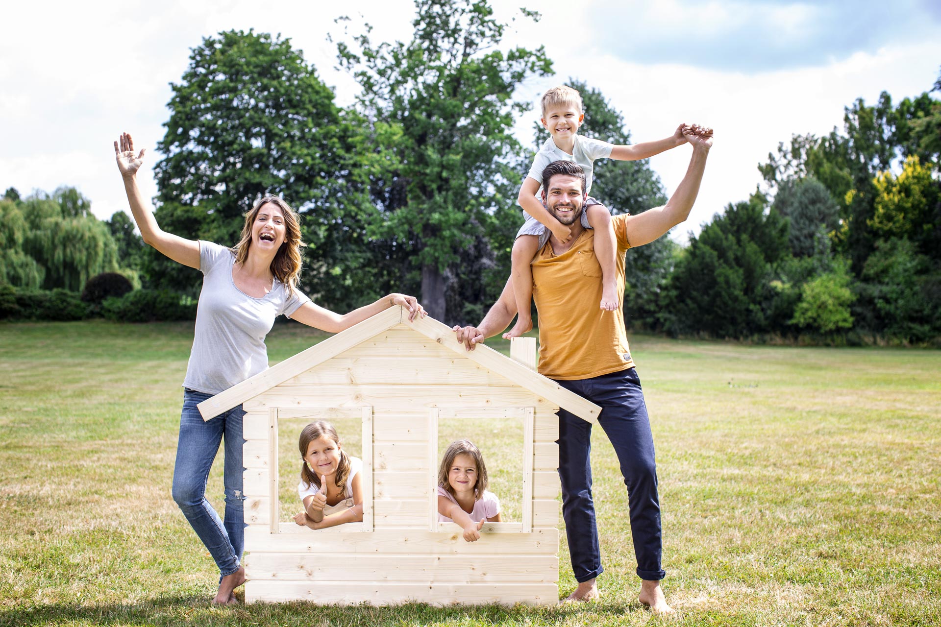 Familie steht mit Holzhaus im Garten.