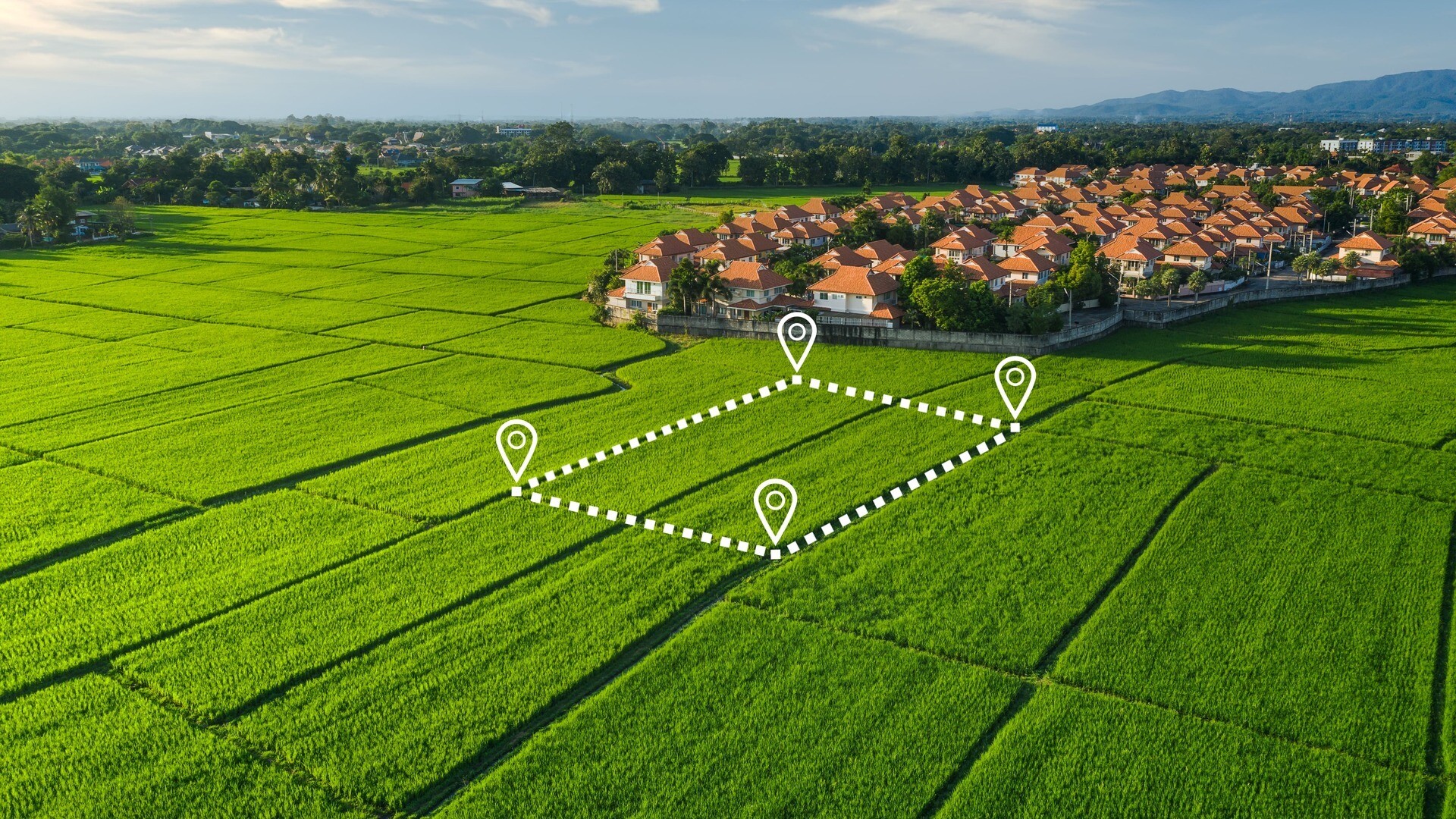 Digital eingezeichnetes Grundstück auf grüner Wiese, im Hintergrund ein kleiner Ort