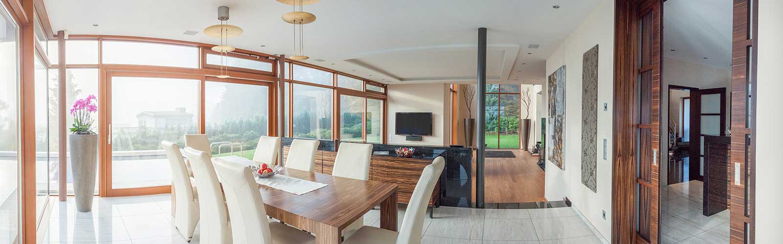 Essbereich mit weißen Stühlen, großen Fenstern und Gartenblick.