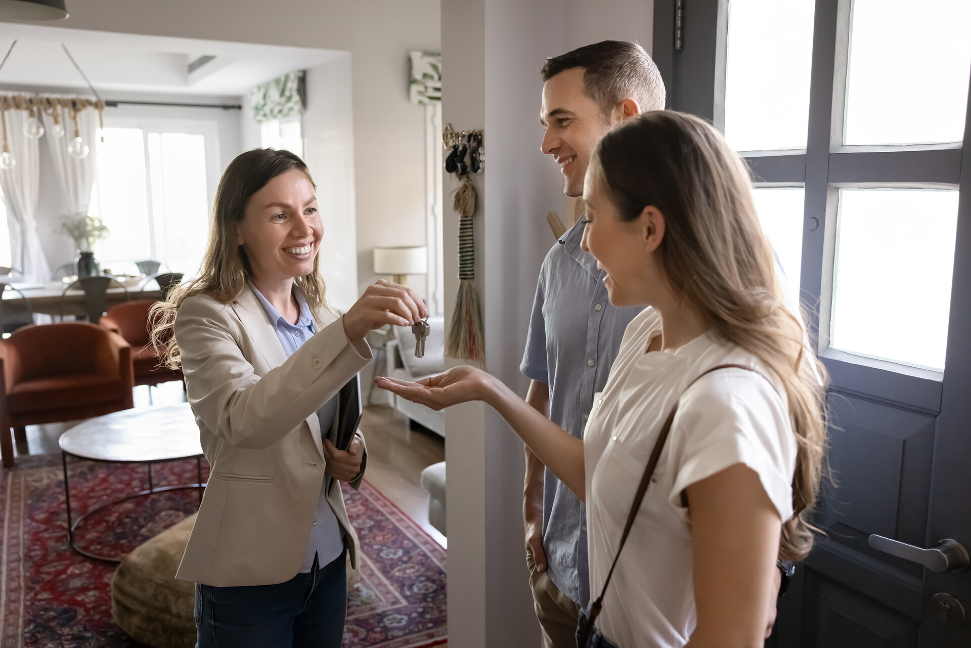 Immobilienmakler übergibt Schlüssel an junges Paar in neuer Wohnung.