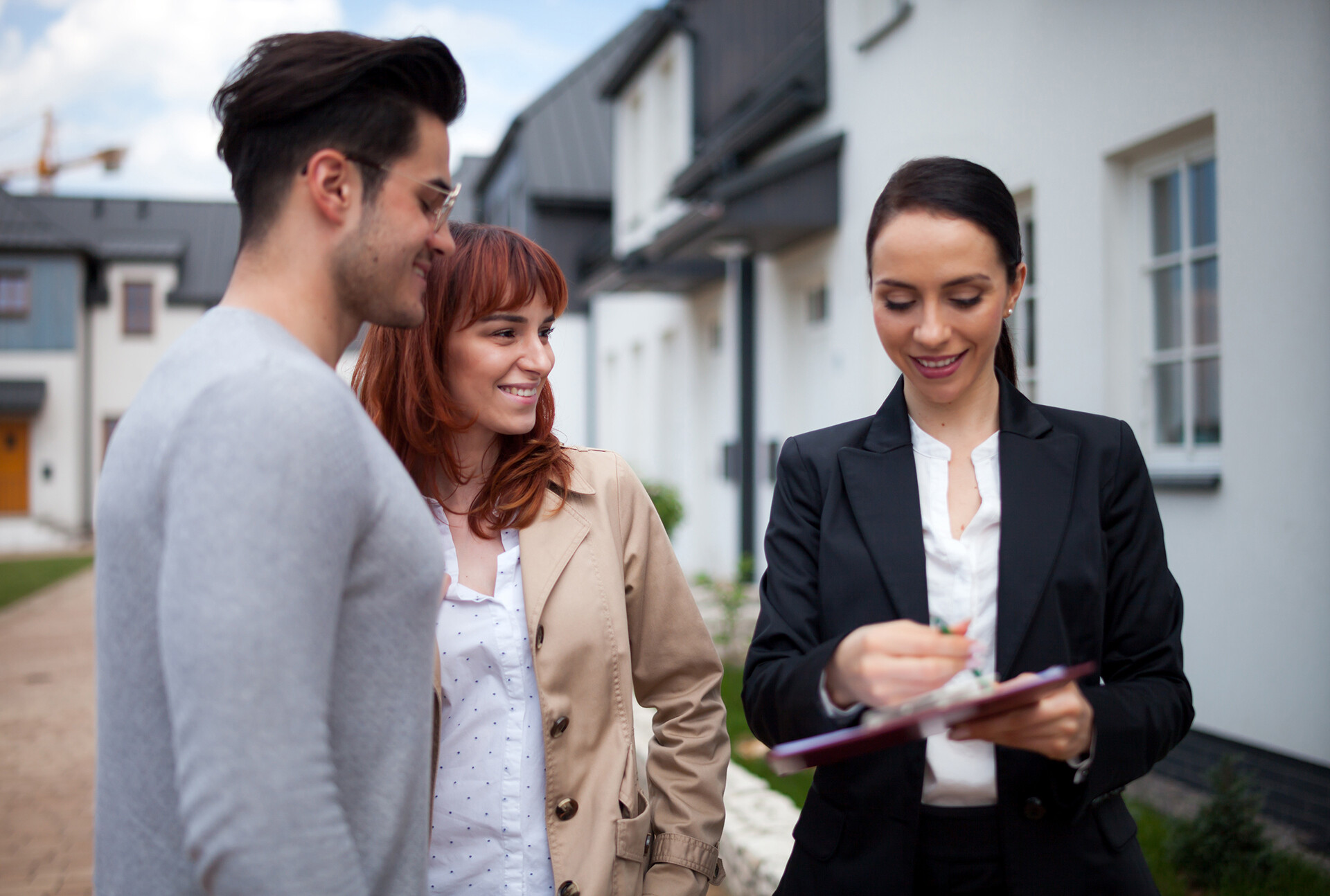 Immobilienmaklerin zeigt jungem Paar Vertrag vor neuem Haus.