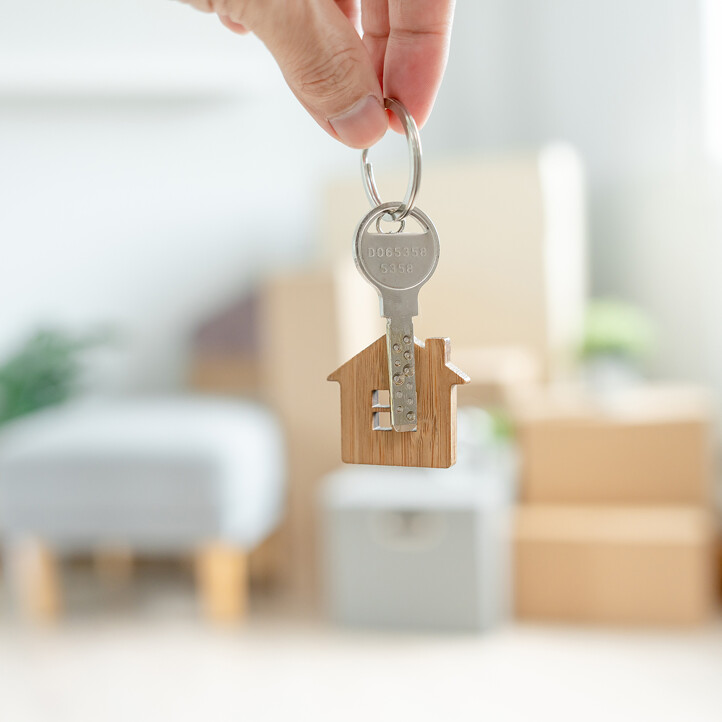 Person hält Hausschlüssel mit Schlüsselanhänger in neuer Wohnung beim Einzug ins neue Zuhause.