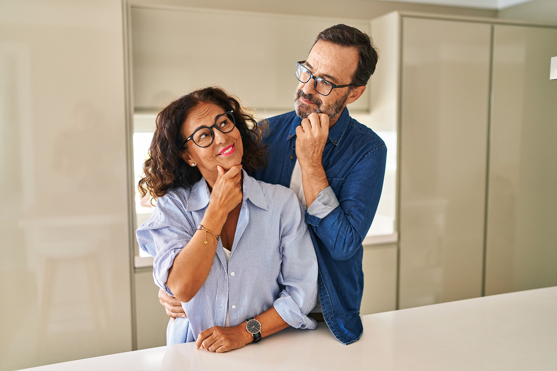 Paar mittleren Alters steht nachdenklich mit Hand am Kinn und überlegt gemeinsam eine Entscheidung.