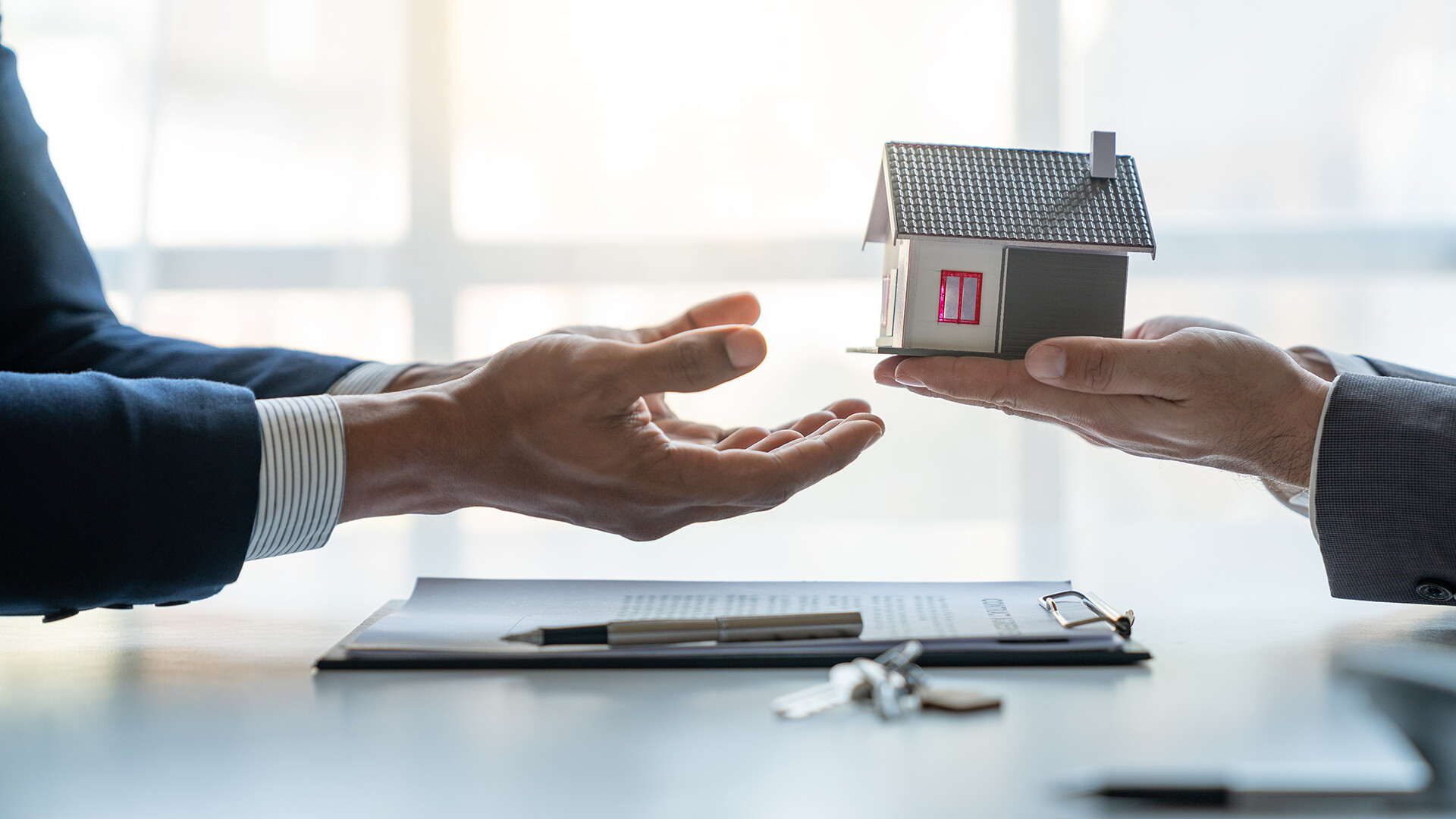 Immobilienmakler übergibt Modellhaus an Kunden nach Vertragsabschluss im Büro.