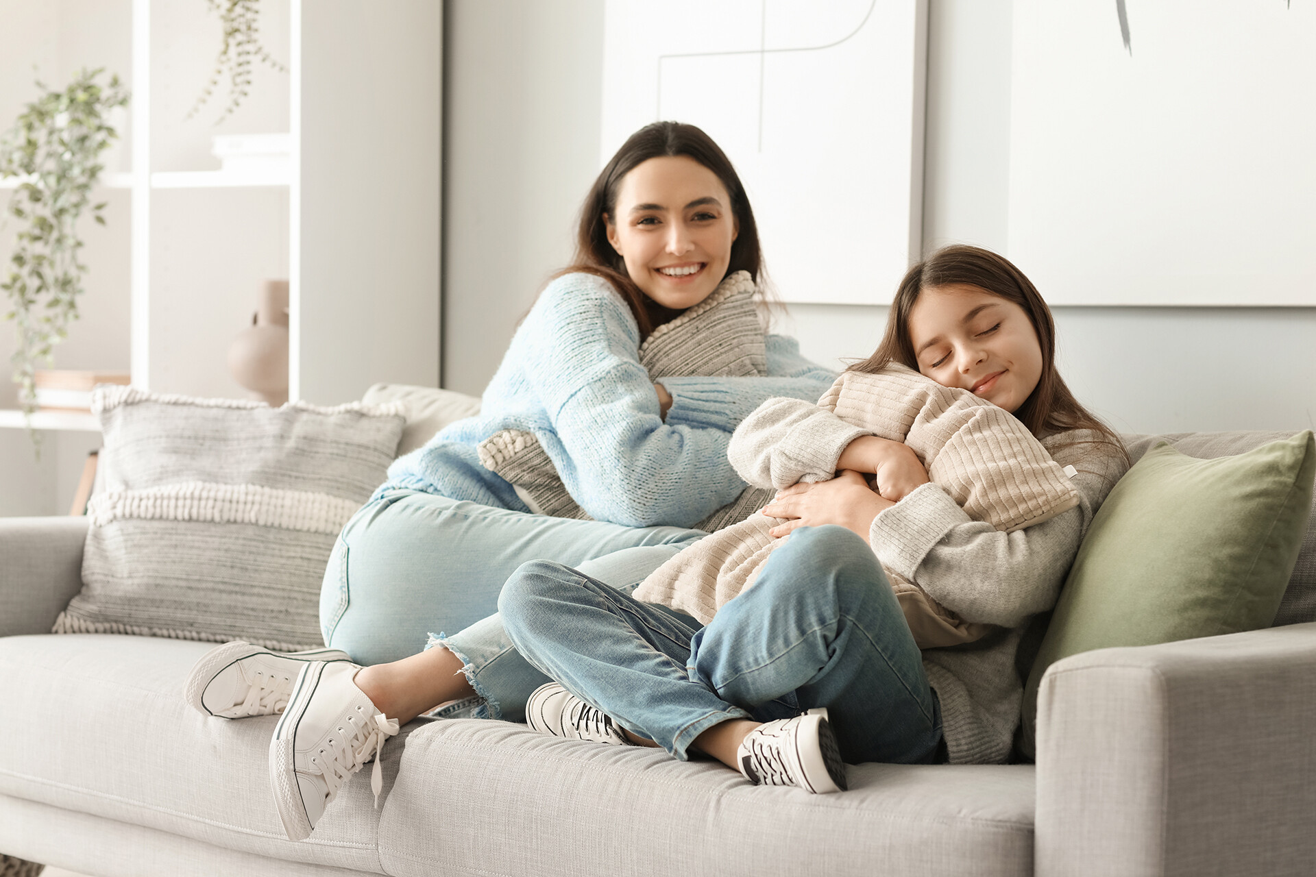 Mutter und kleine Tochter sitzen mit Kissen auf dem Sofa im Wohnzimmer.