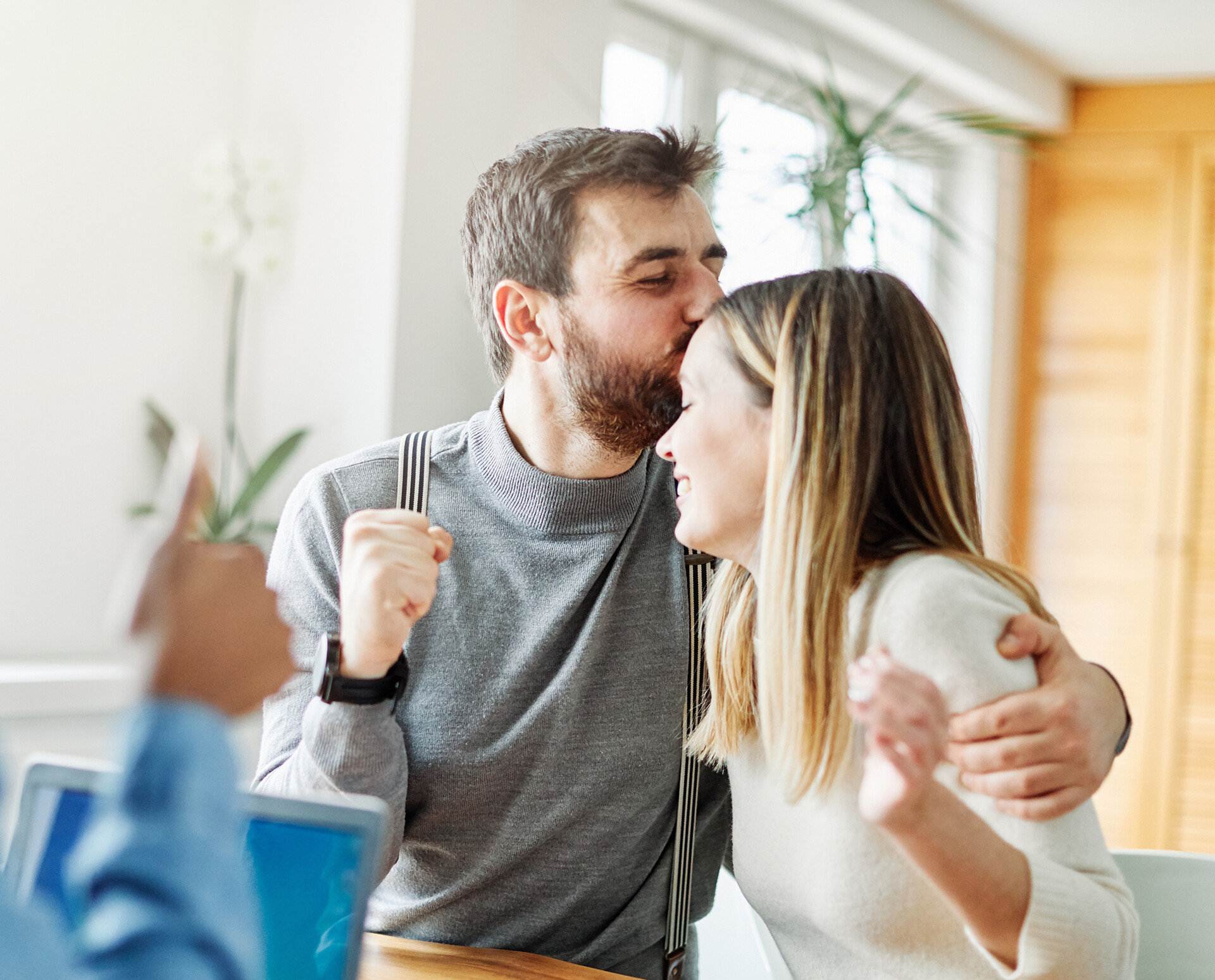 Paar feiert gemeinsam mit Immobilienmakler den erfolgreichen Abschluss eines Hauskaufs im Büro.