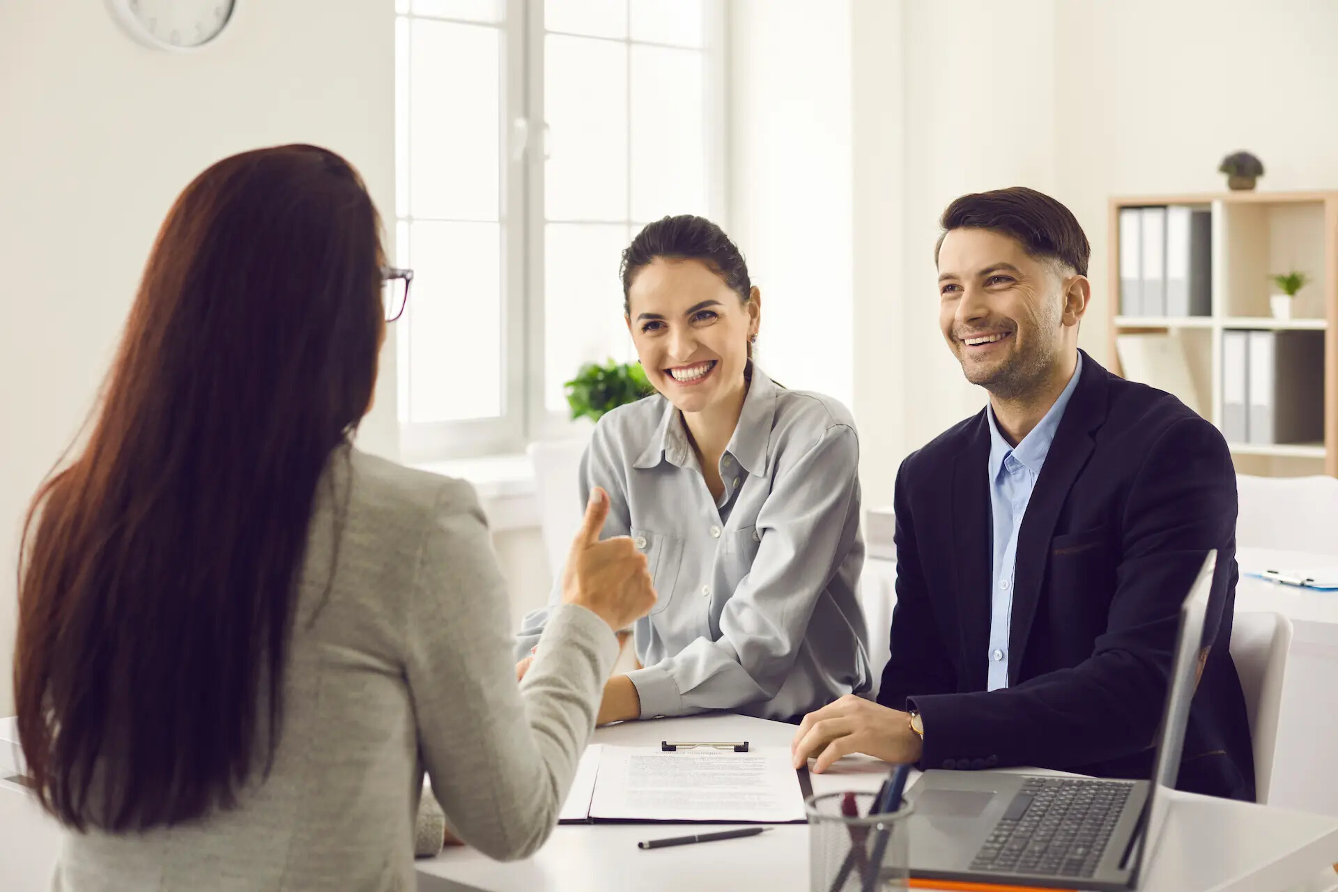 Beraterin zeigt Daumen hoch im Gespräch mit jungem Paar.