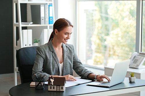 Maklerin sitzt lächelnd am Laptop im Büro.