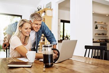 Paar im mittleren Alter sitzt mit Laptop und Unterlagen zu Hause und plant Immobilienentscheidungen.