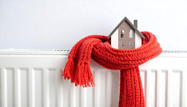 Modellhaus auf Heizung eingehüllt in rotem Schal.