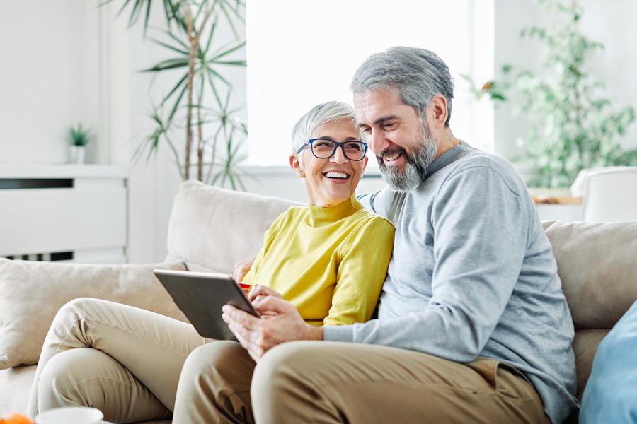 Lachendes Seniorenpaar auf der Couch mit Tablet in der Hand.