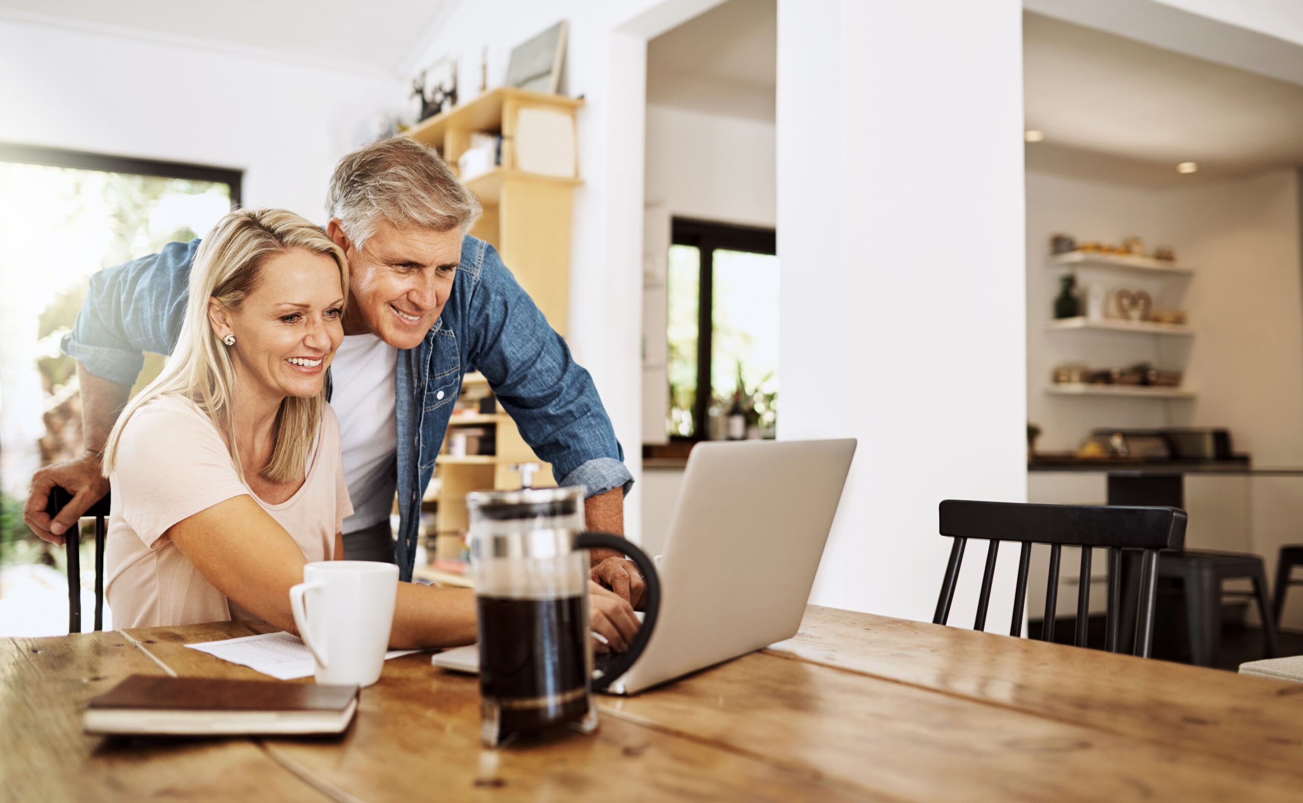 Paar im mittleren Alter sitzt mit Laptop und Unterlagen zu Hause und plant Immobilienentscheidungen.