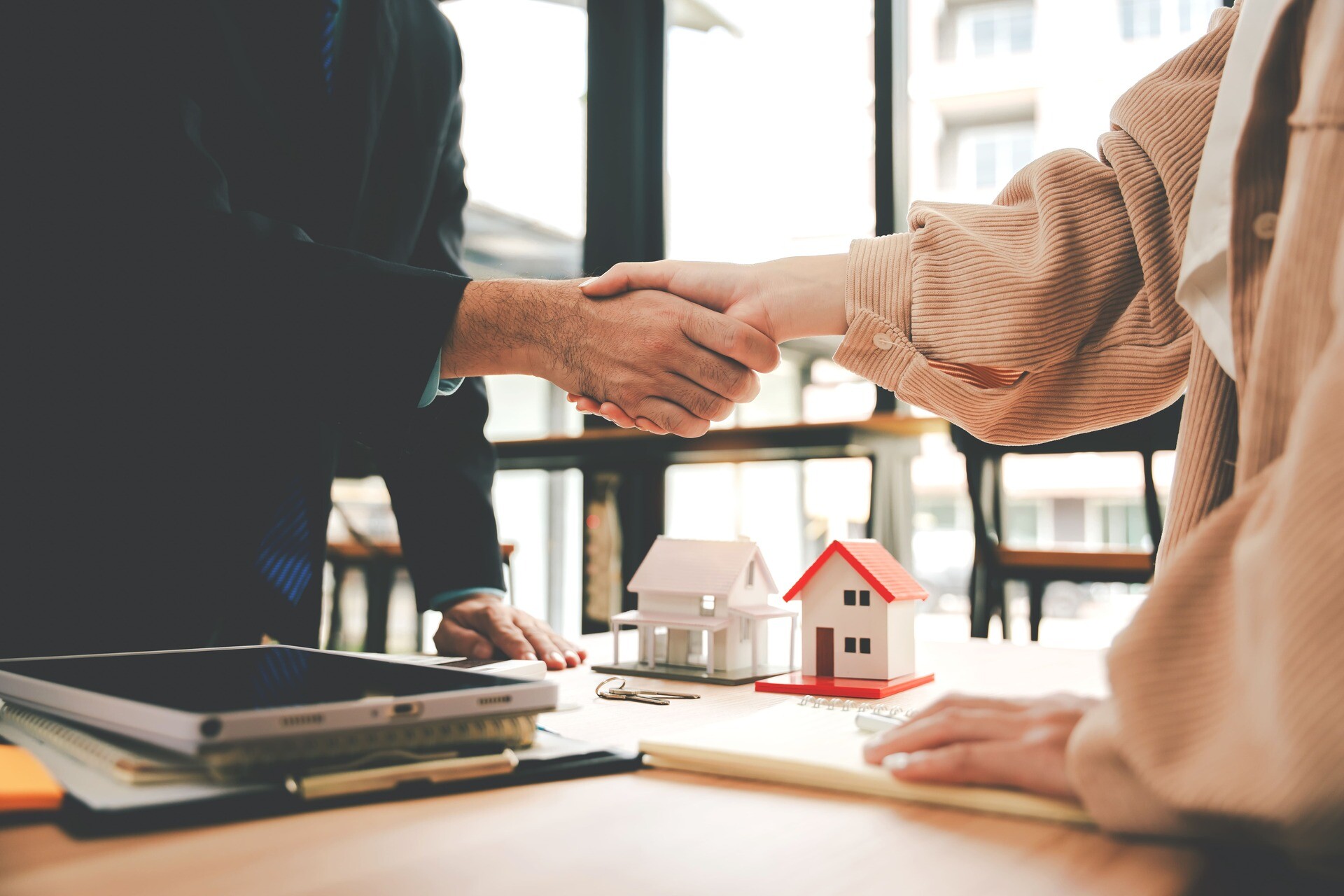 Zwei Personen reichen sich vor Modellhäusern die Hand am Schreibtisch.
