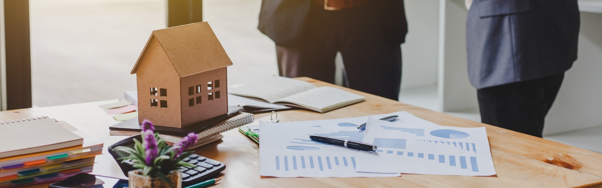 Hausmodell auf Schreibtisch neben Unterlagen
