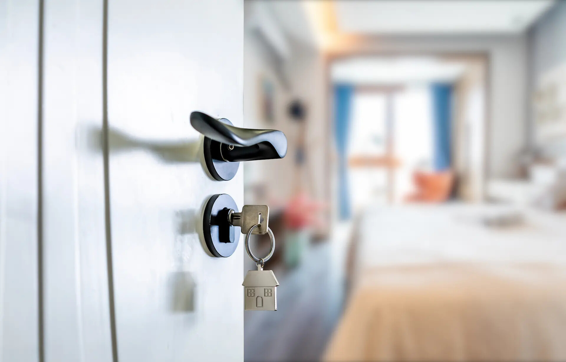 Die Tür mit Schlüssel und Schlüsselanhänger in Form eines Hauses führt zu einem hellen Schlafzimmer.