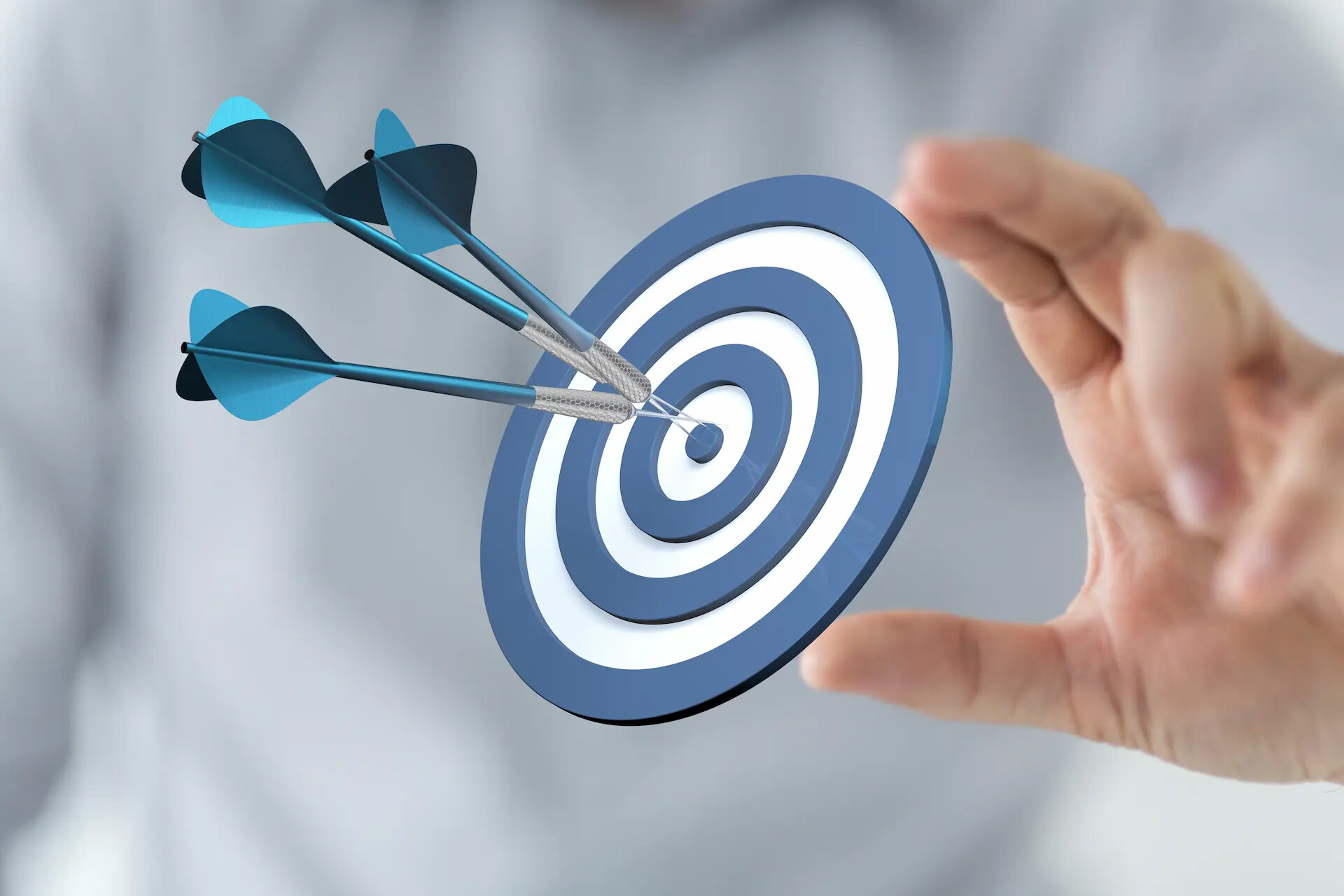 Hand hält Zielscheibe mit drei Pfeilen im Mittelpunkt.