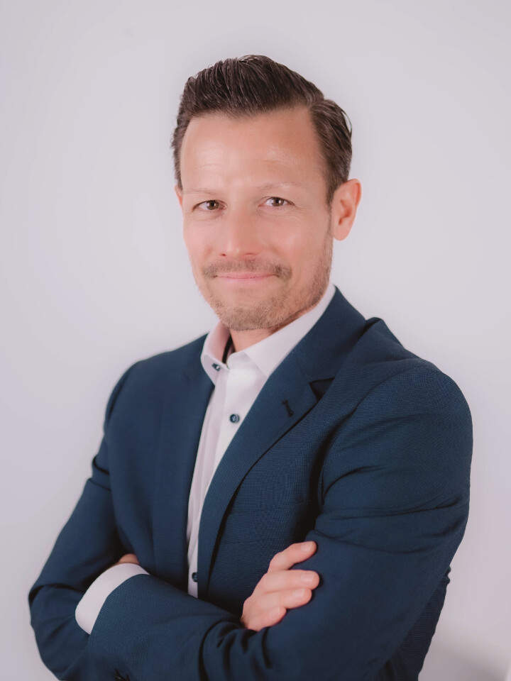 Mann im blauen Anzug, verschränkte Arme, leichtes Lächeln.