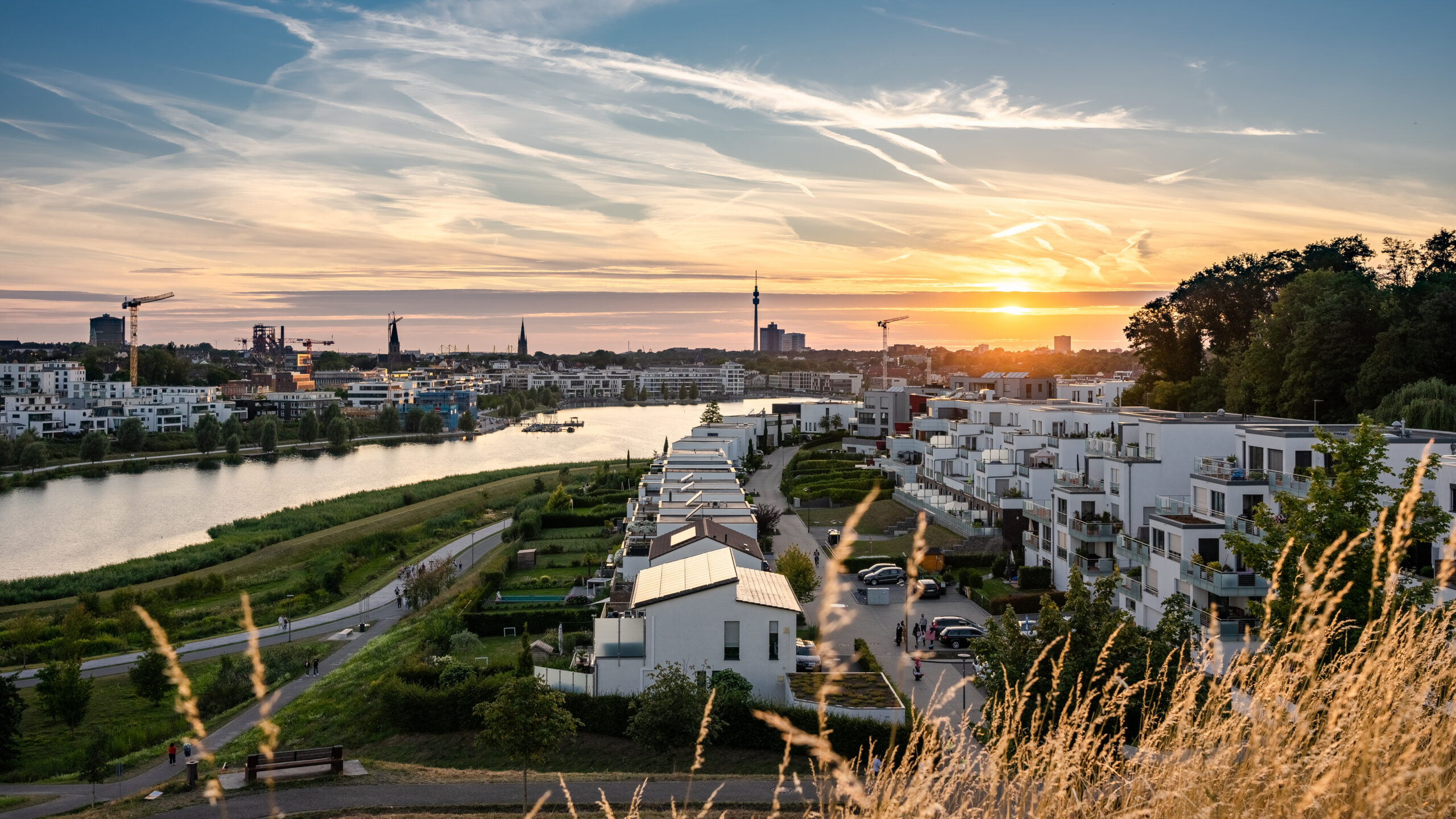Wohnungen am Flussufer, Grünanlagen, Sonnenuntergang, Skyline der Stadt, Wasser.