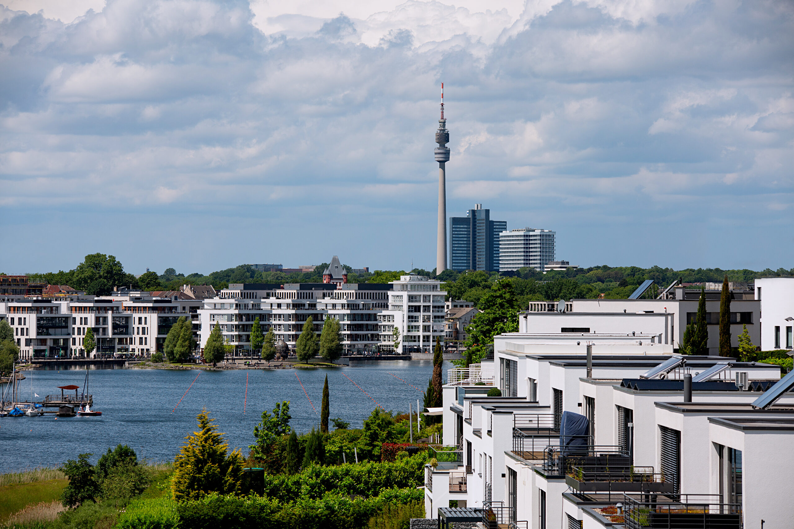 Waterfront buildings, TV tower, cityscape, partly cloudy sky.