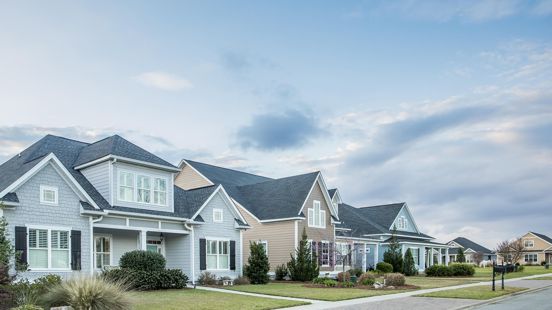 Moderne Vorstadthäuser mit gepflegten Vorgärten bei Wolkenhimmel.