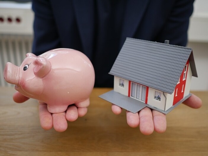 Modellhaus mit Sparschwein in Händen