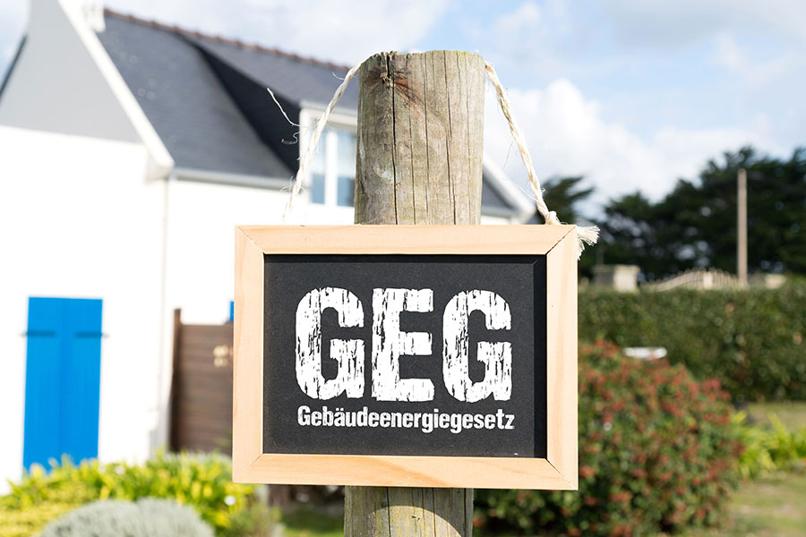 Schild mit Aufschrift "GEG - Gebäudeenergiegesetz" hängt an einem Zaunpfahl