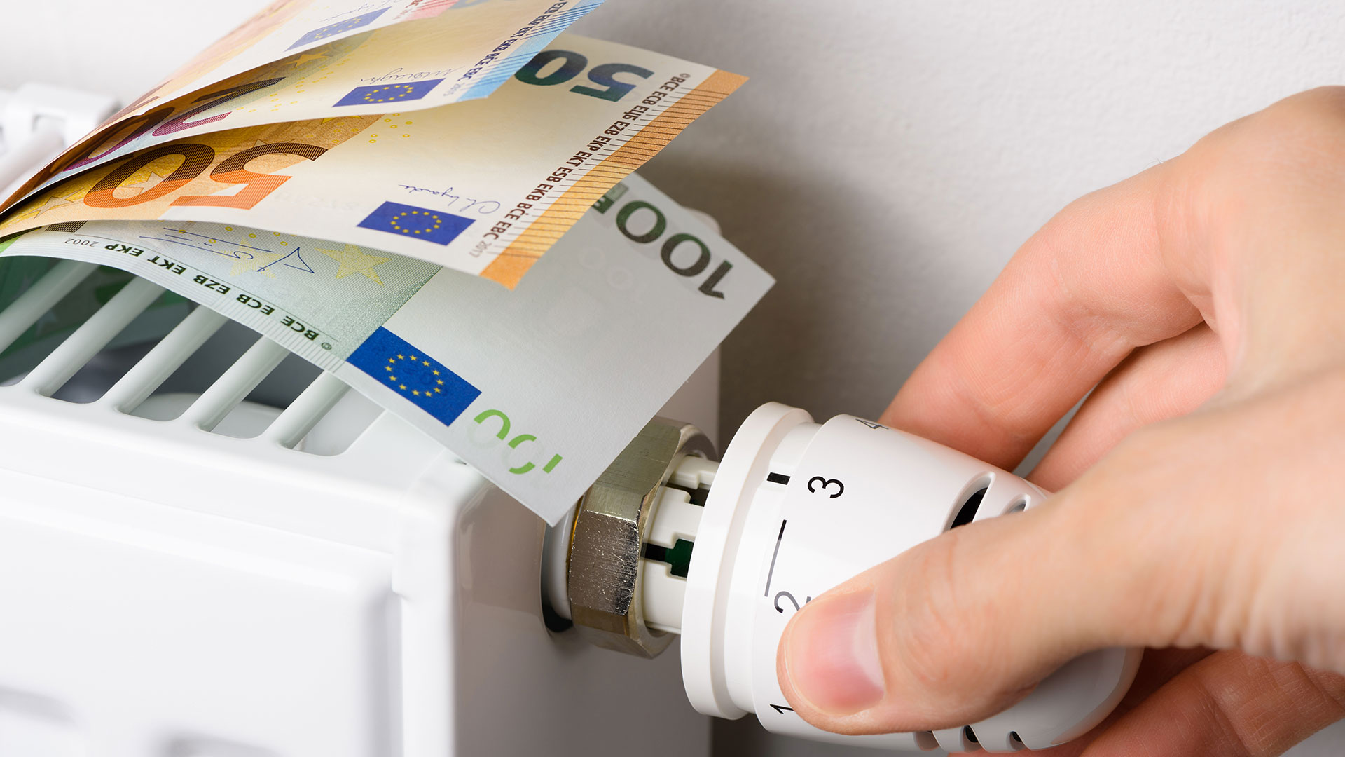 Gelscheine liegen auf einer Heizung, eine Hand dreht am Thermostat