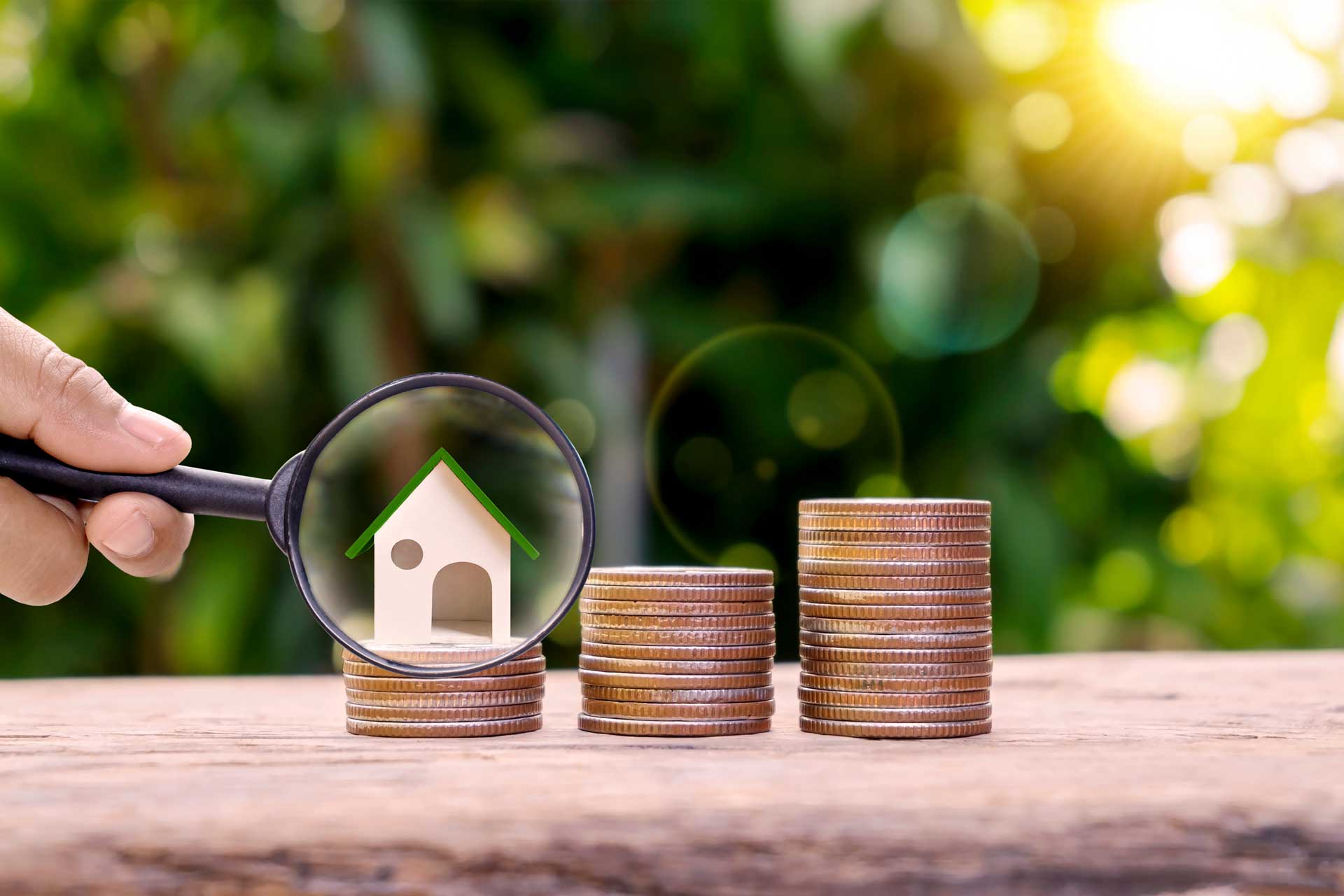 Lupe vor Modellhaus auf einem Münzstapel: Wertermittlung vor dem Verkauf
