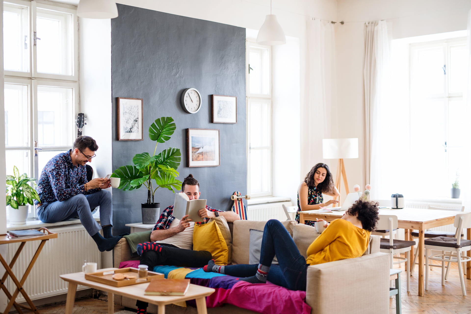 Vier Personen lesen und nutzen Geräte im hellen Wohnzimmer.