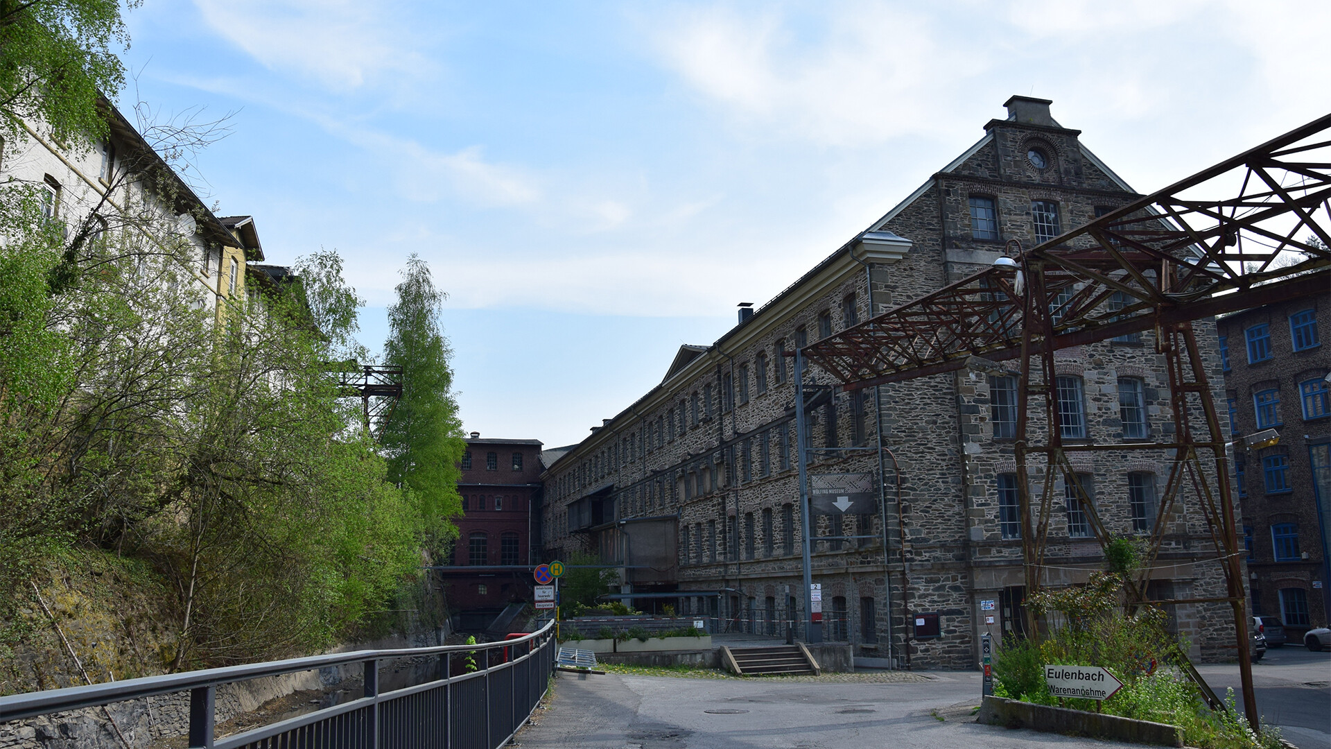 Industriebauten aus Stein und Backstein mit Bewuchs und Steg.