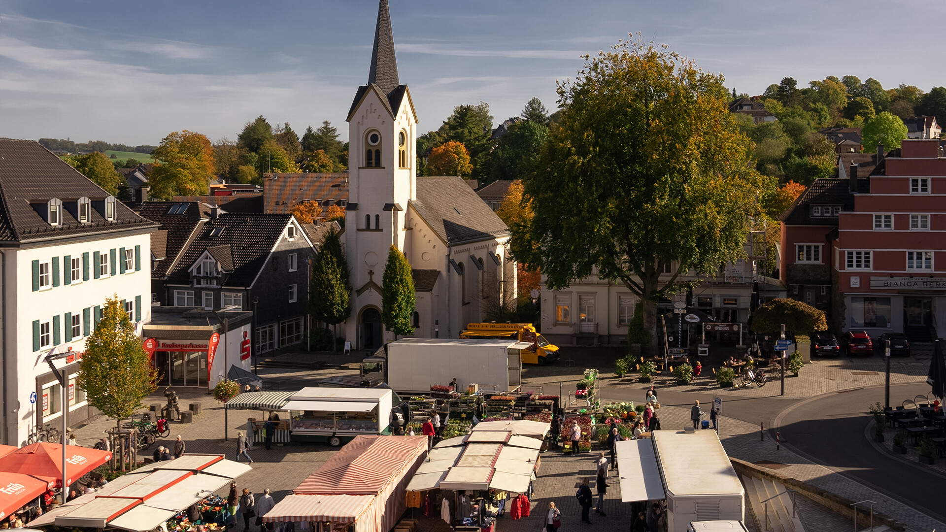Stadtplatz mit Marktständen, Menschen und Kirche im Grünen.