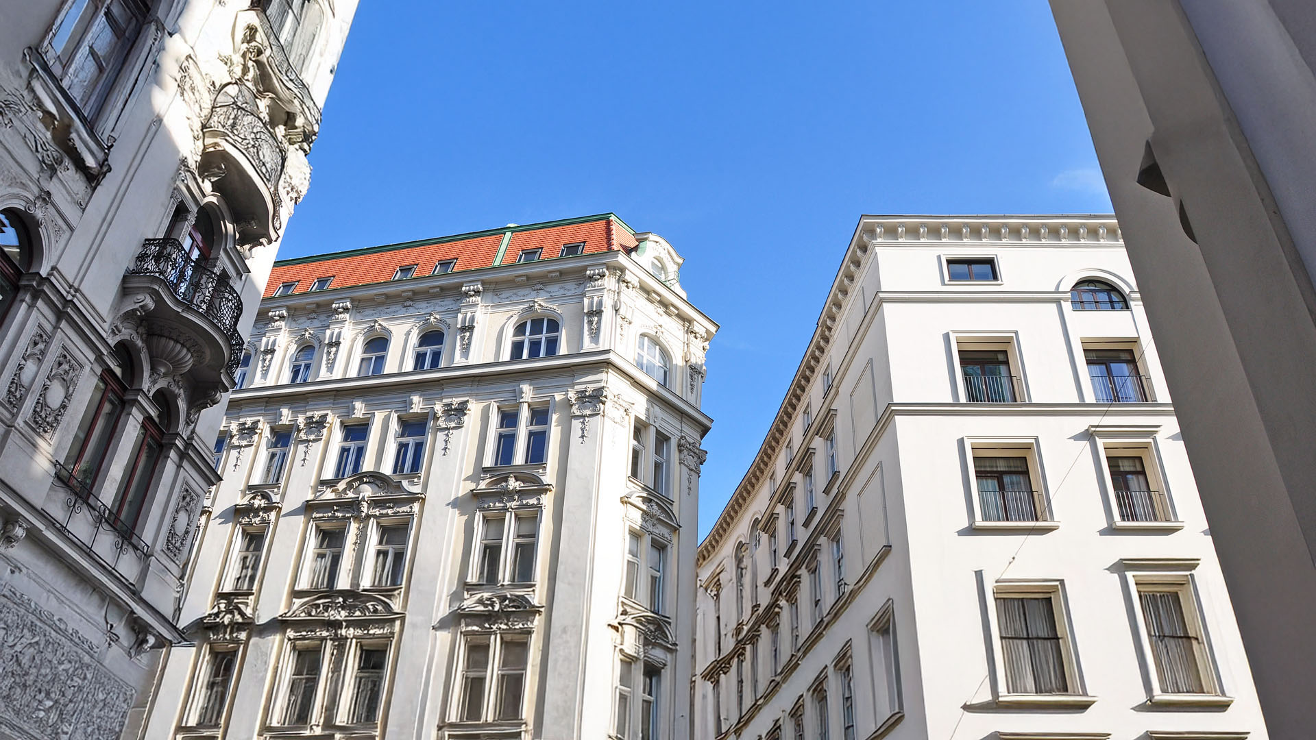 Verschnörkelte weiße Gebäude mit vielen Fenstern unter einem blauen Himmel, von unten gesehen.