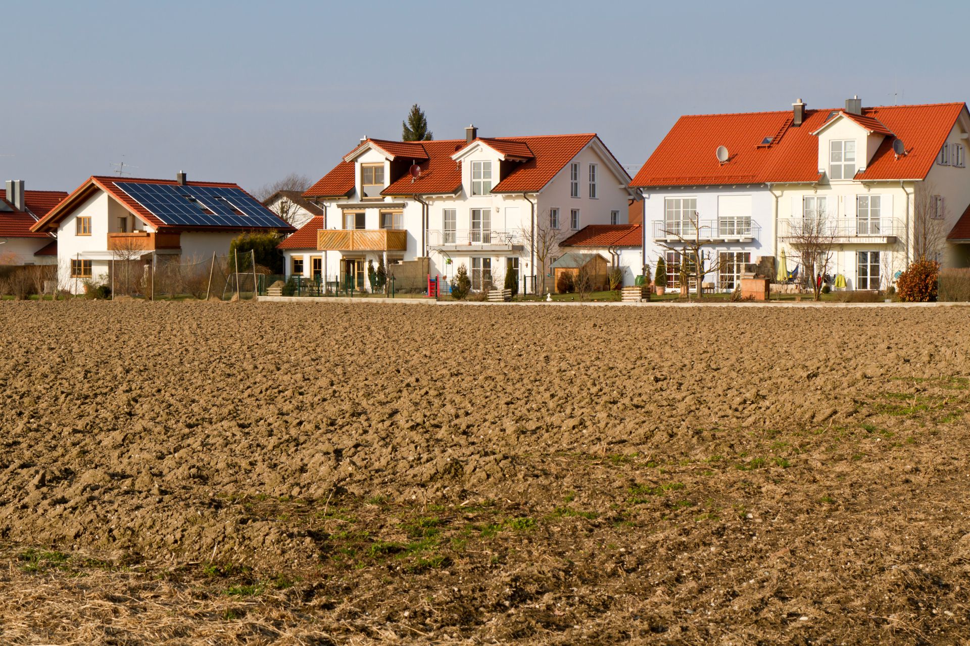 Moderne Häuser mit roten Dächern hinter leerem, gepflügtem Feld.