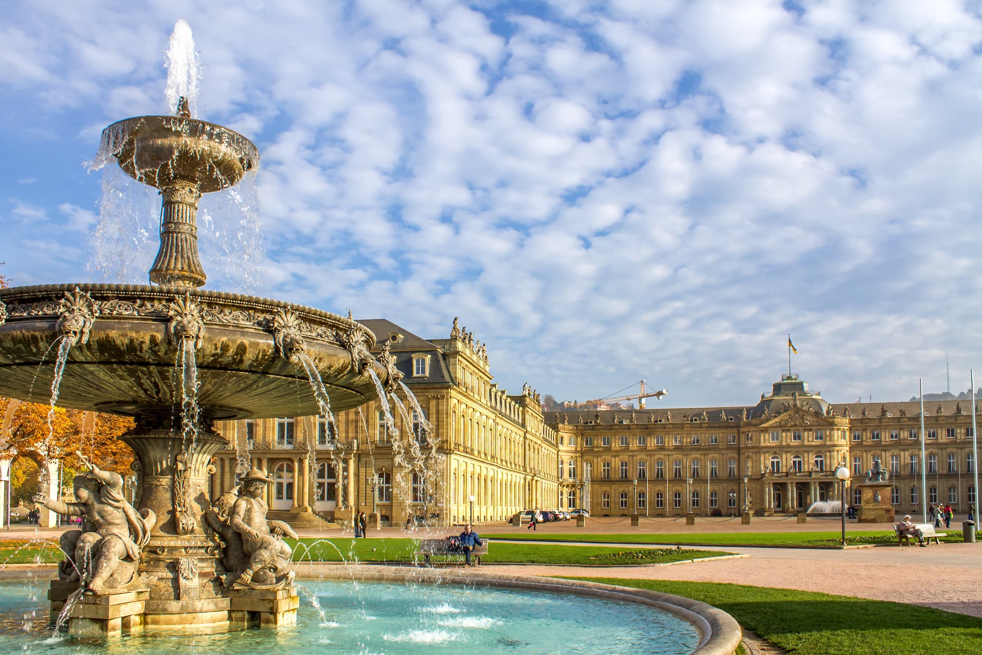 Springbrunnen mit Statuen vor historischem Palast unter blauem Himmel.