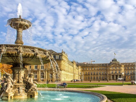 Springbrunnen mit Statuen vor historischem Palast unter blauem Himmel.