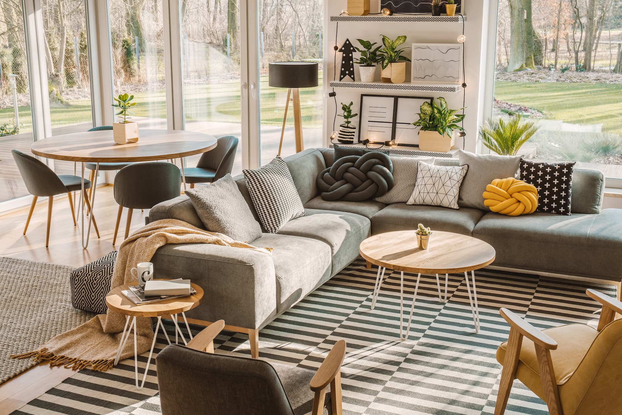 Wohnzimmer mit grauem Sofa, runden Tischen und großen Fenstern.