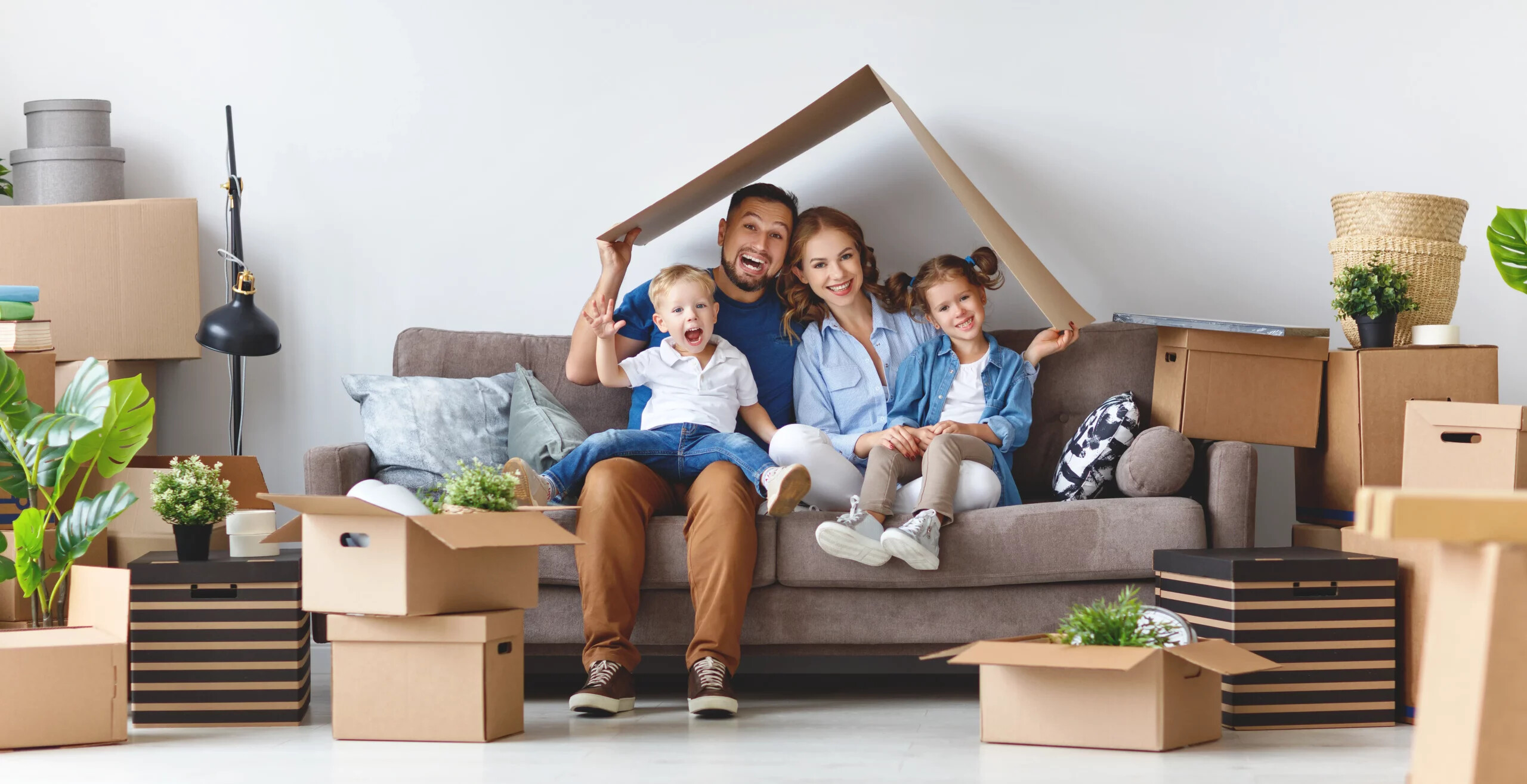 Familie sitzt auf dem Sofa mit Kartondach, Umzugskartons drumherum.