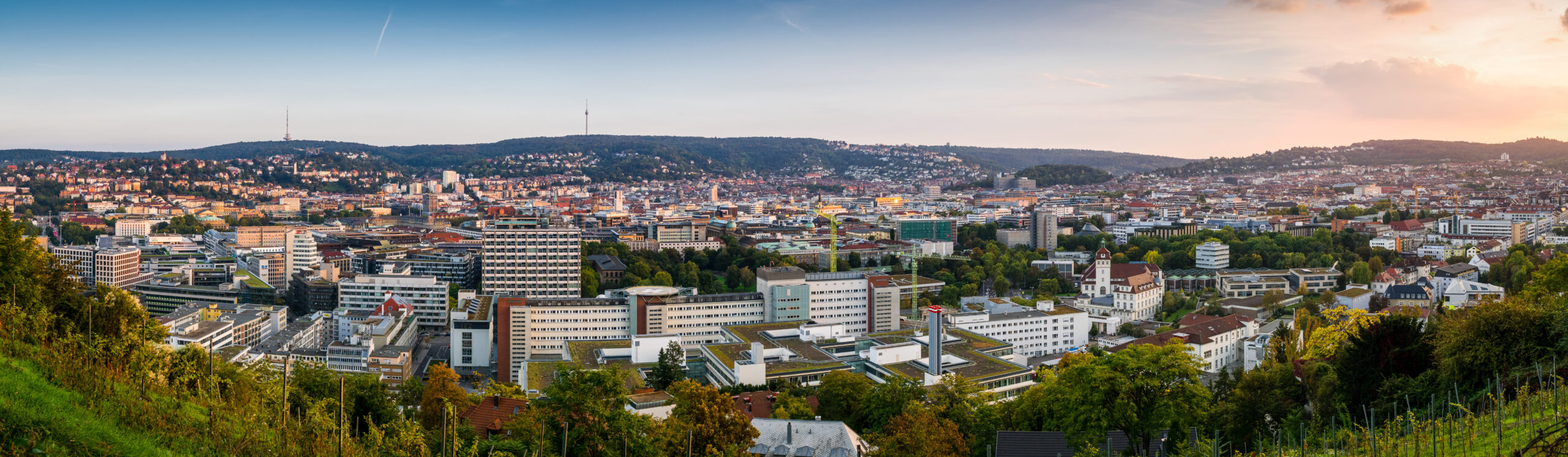 Stuttgart mit Gebäuden, Hügeln und Grün unter Wolken.