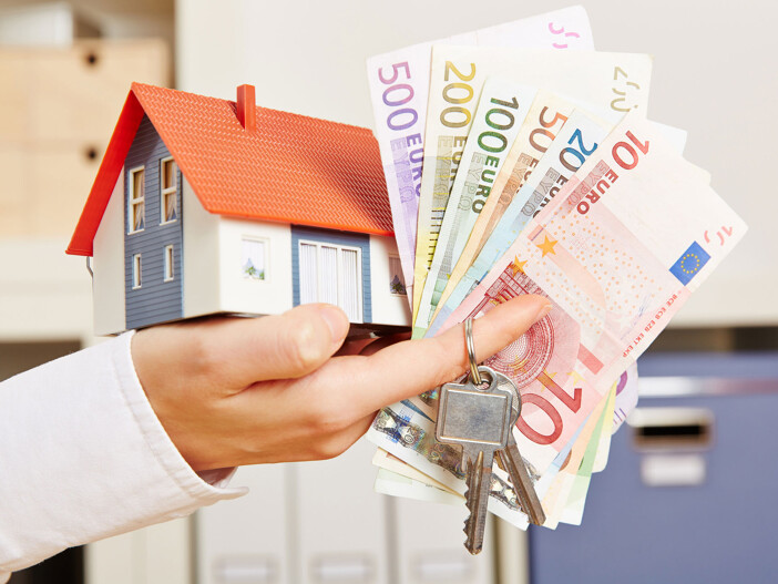Person hält Modellhaus mit Geldscheinen und Schlüssel in der Hand