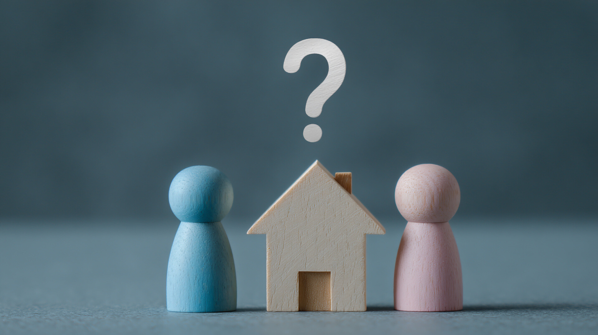 Holzfiguren mit Hausmodell und Fragezeichen