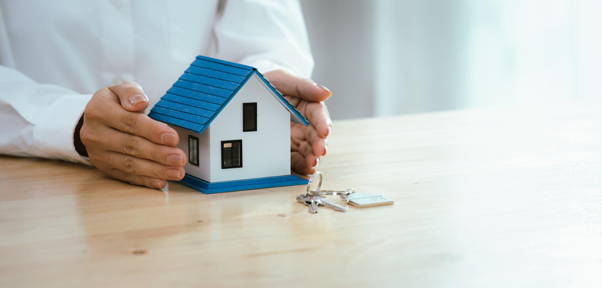 Frau hält ihre Hände schützend um ein Hausmodell