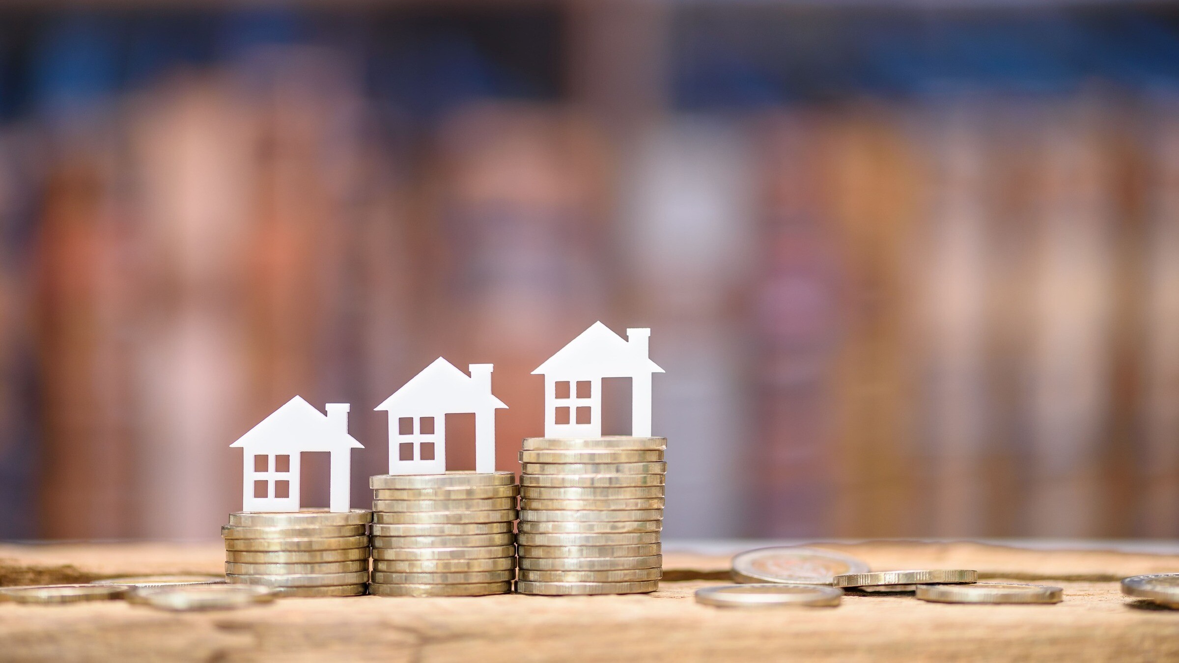 Kleine Modellhäuser stehen nebeneinander auf Münzstapeln, stehen symbolisch für die Nebenkosten beim Immobilienkauf