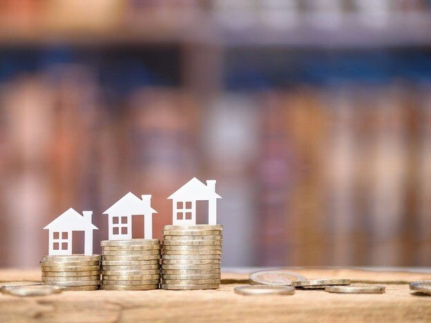 Kleine Modellhäuser stehen nebeneinander auf Münzstapeln, stehen symbolisch für die Nebenkosten beim Immobilienkauf