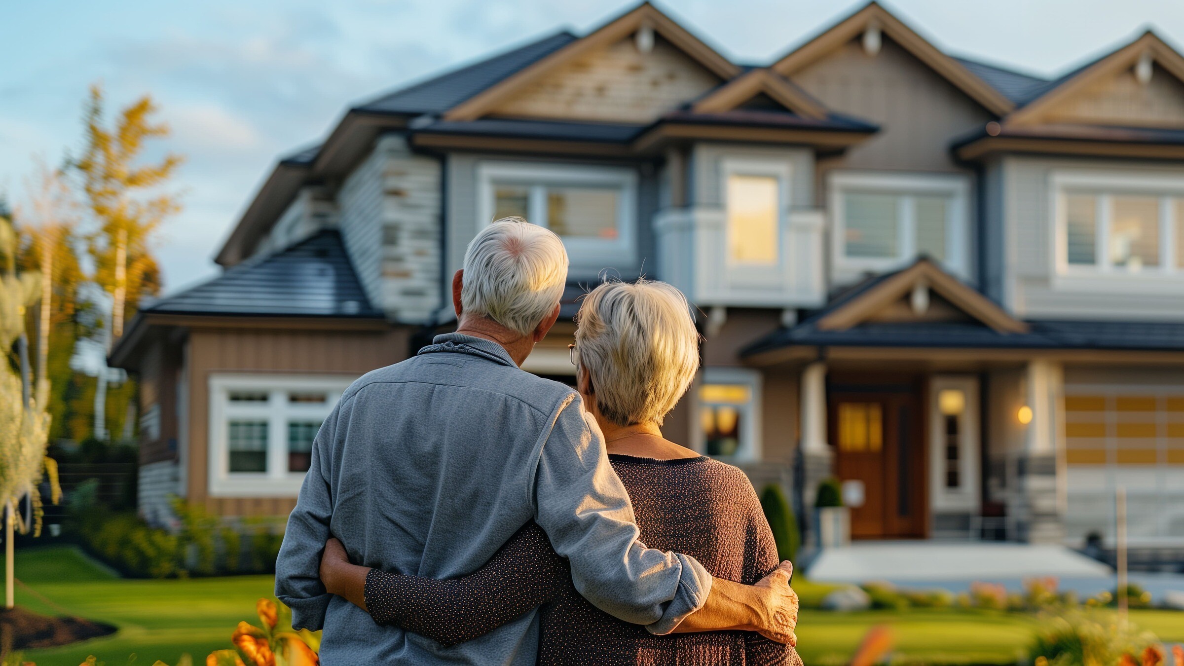 Ältere Eigentümer einer Immobilie stehen Arm in Arm vor ihrem Haus