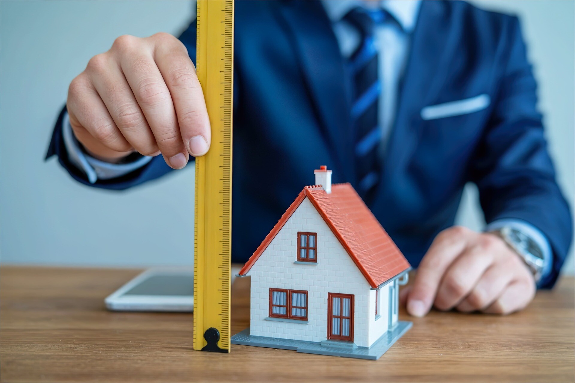 Mann hält Maßband neben Modellhaus