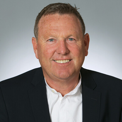 Hans-Peter Klus im dunklen Blazer und weißem Hemd vor grauem Hintergrund.