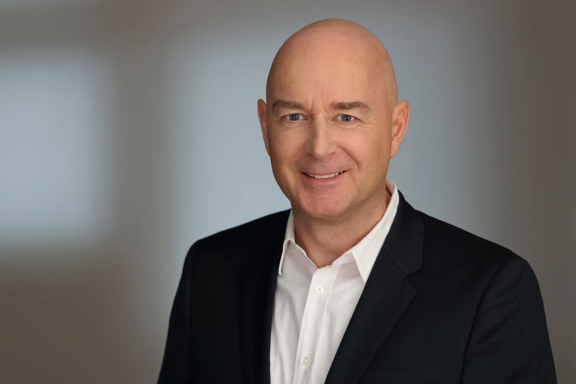 Thomas Lambert im schwarzen Anzug lächelt vor einem unscharfen Hintergrund.