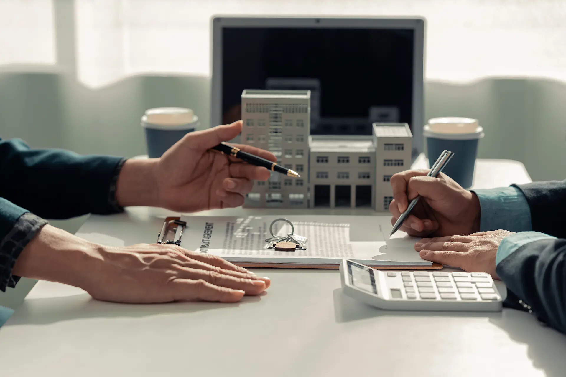 Zwei Personen unterschreiben Dokumente am Tisch mit Modellen und Laptop.