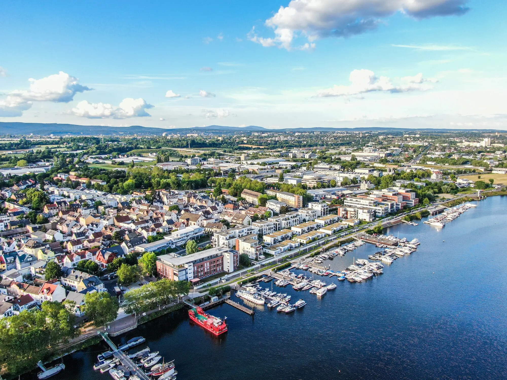 Stadt am Fluss mit Jachthafen, Booten und Häusern im Grünen.